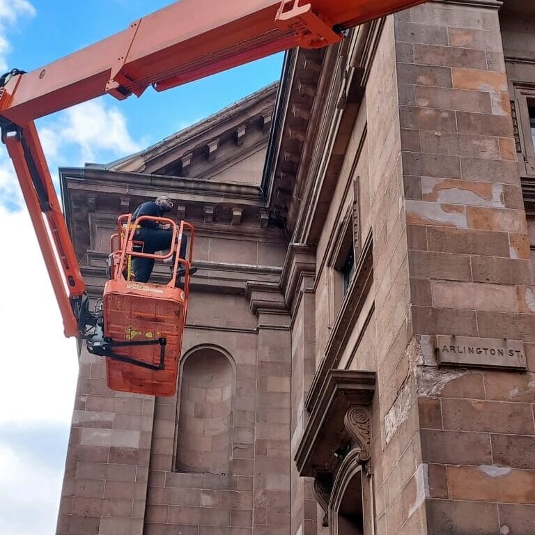 Photo of a man in a cherry picker next to and old stone church.