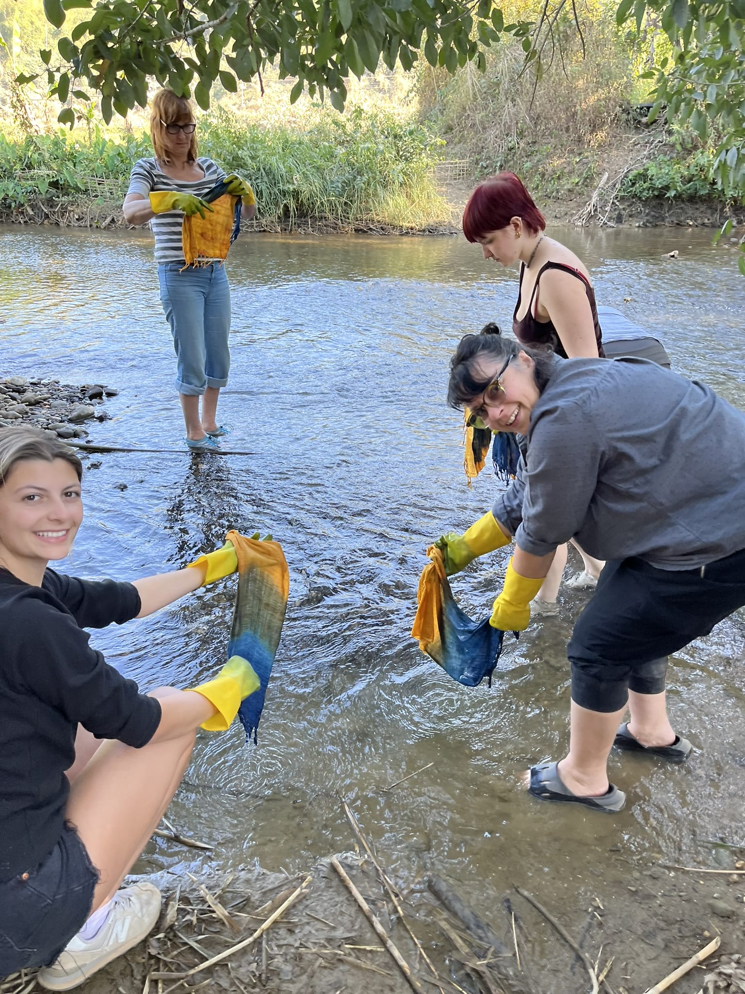 Four people stand near a stream rinsing dyed garments.