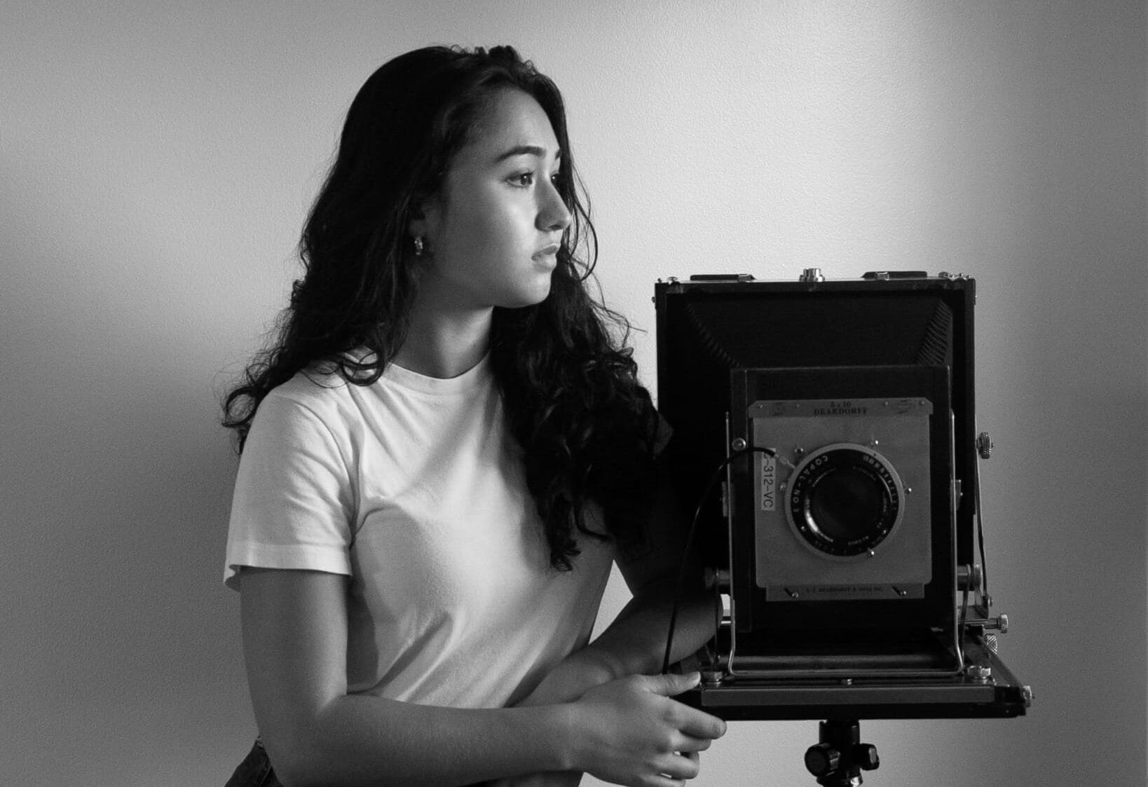 Woman stands with camera.