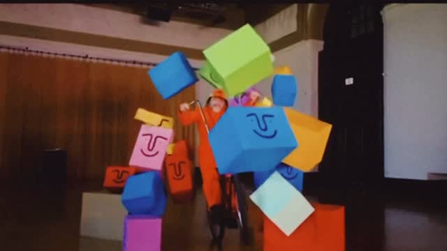 A man on a bike breaks through a pile large of colorful boxes with smiley faces on them.