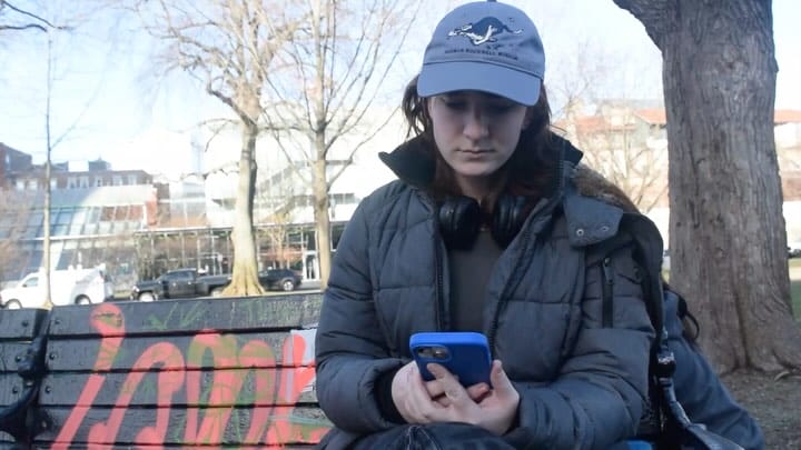 A woman sits on a park bench looking at her phone