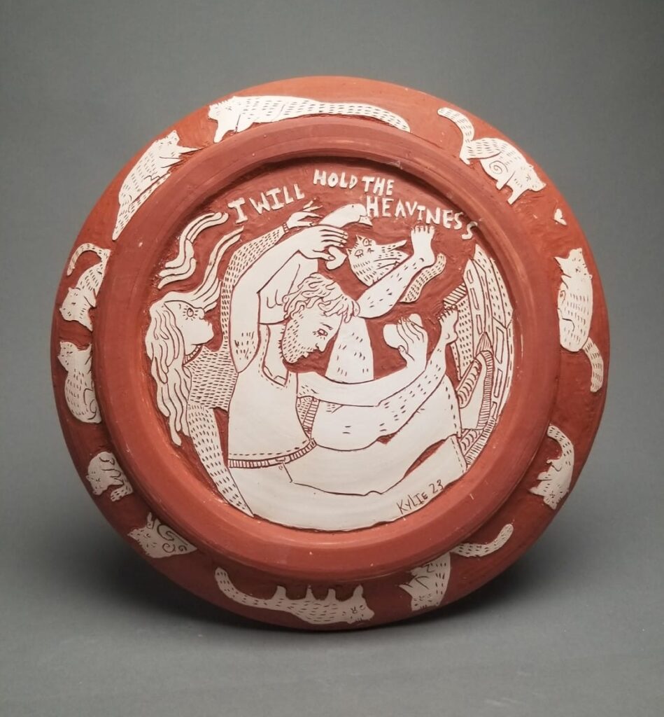 A red underglazed ceramic bowl with carved white illustrations on it.