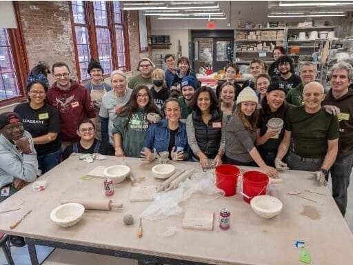 A group of ceramics students and community members gather around a table.