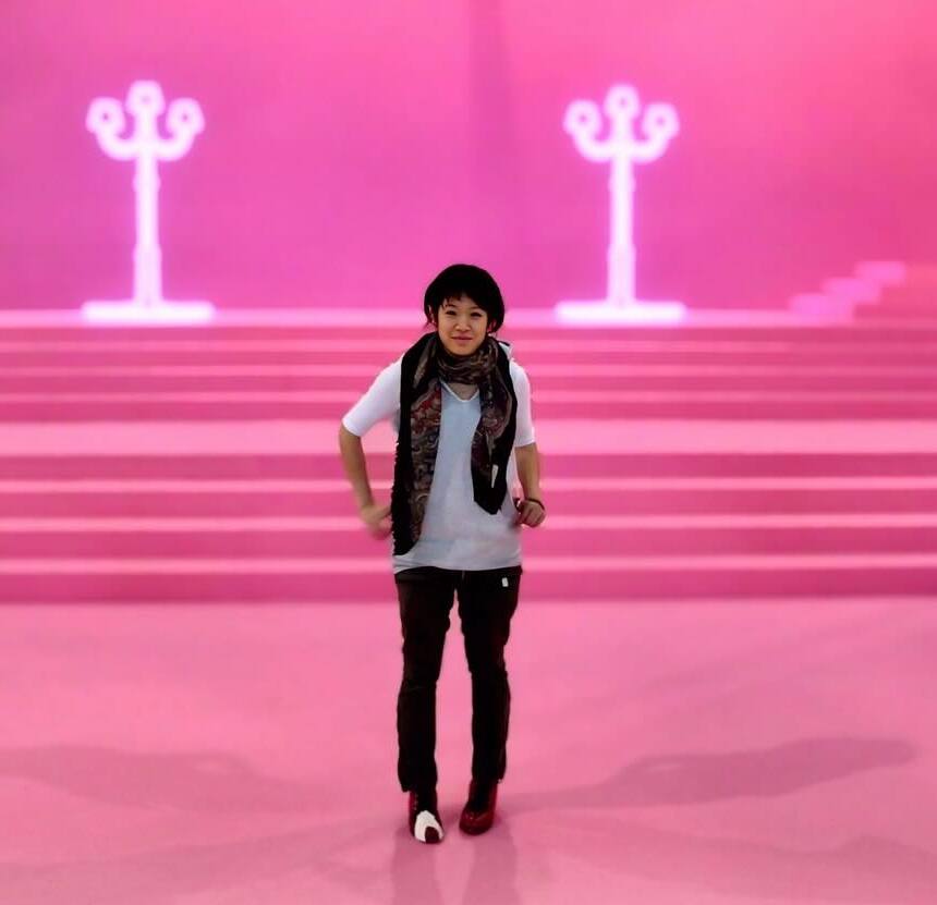 A woman wearing a scarf and white t shirt stands on a hot pink sound stage.