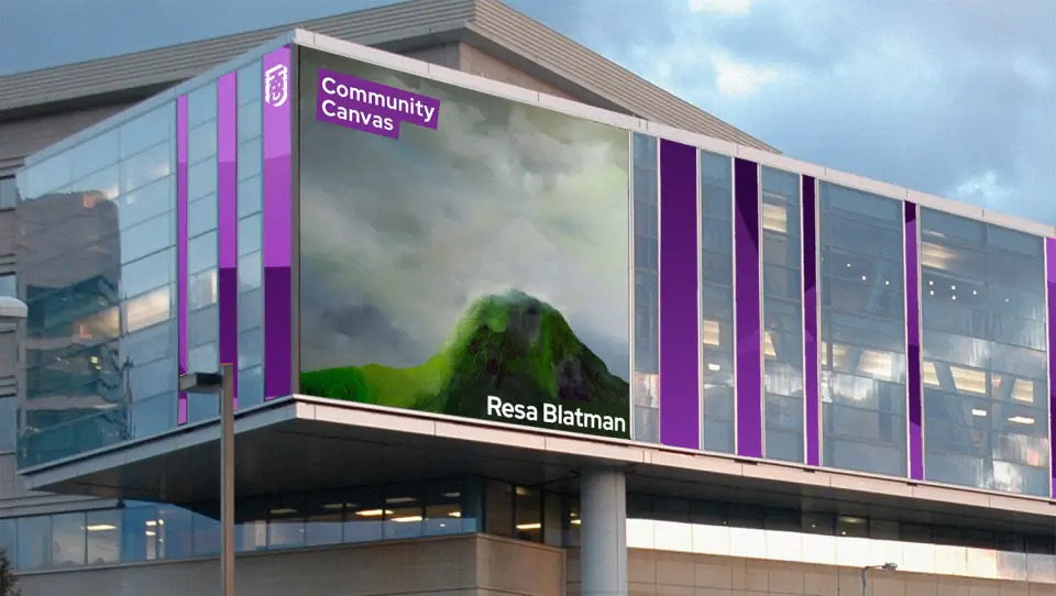 A digital art display on a modern building showcases Beauteous Heap—a green mountain beneath a cloudy sky.