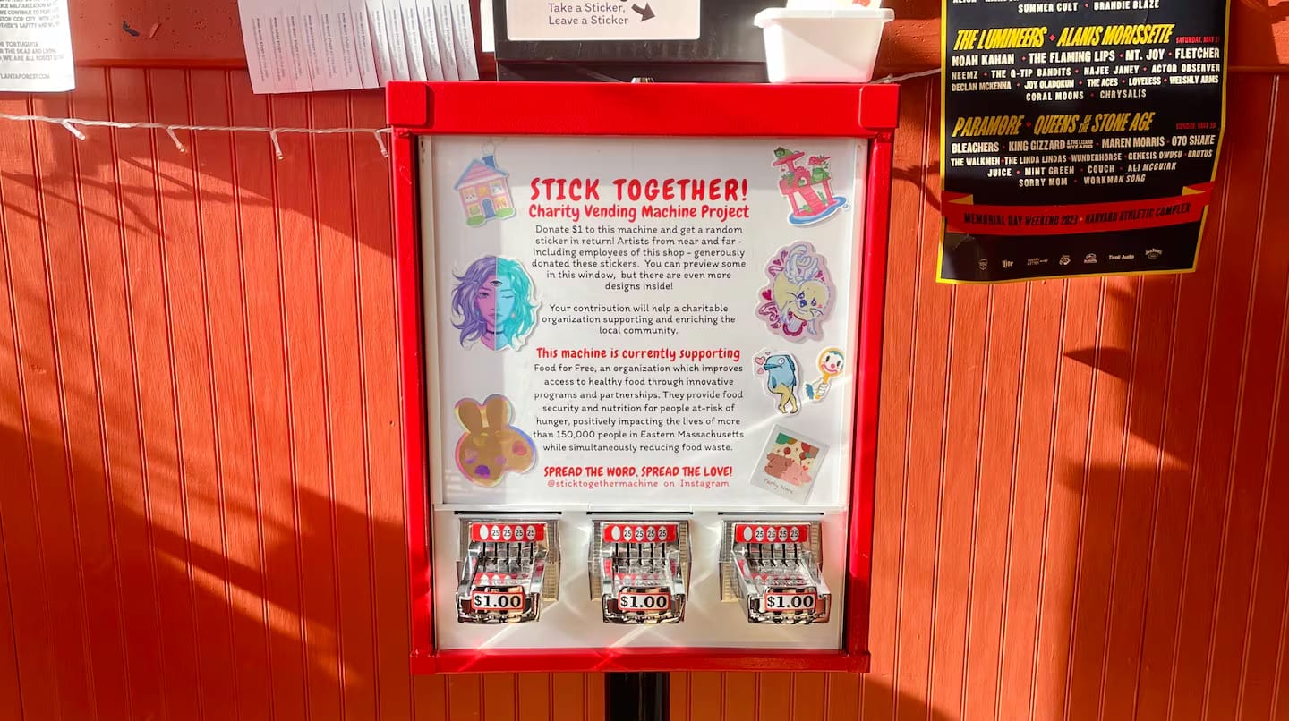 The vibrant red charity sticker vending machine, dubbed Stick Together!, is adorned with colorful designs and supports a community mission.