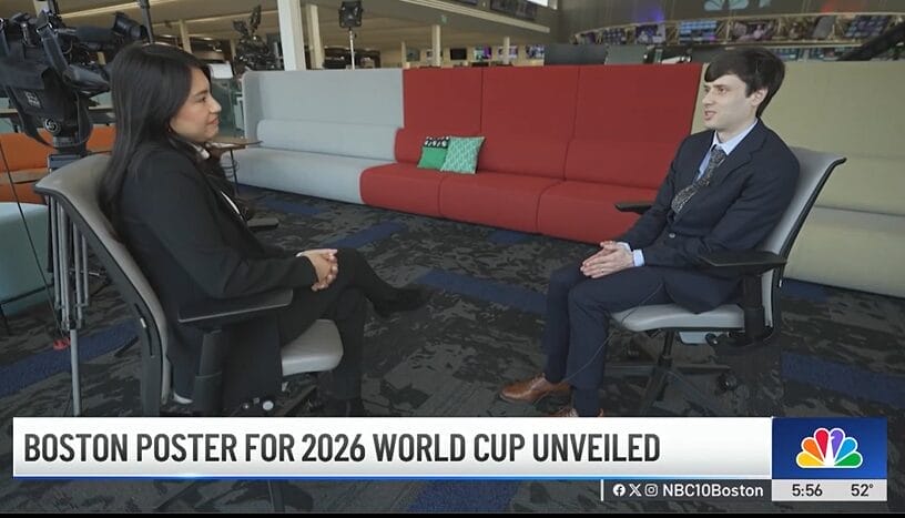 Two people are seated in an open office, engaged in conversation. A red sofa with green cushions sits behind them. Below, a news banner reads: Boston Poster for 2026 World Cup Unveiled. The NBC10 Boston logo is visible, highlighting Boston as a vibrant host city for the event.