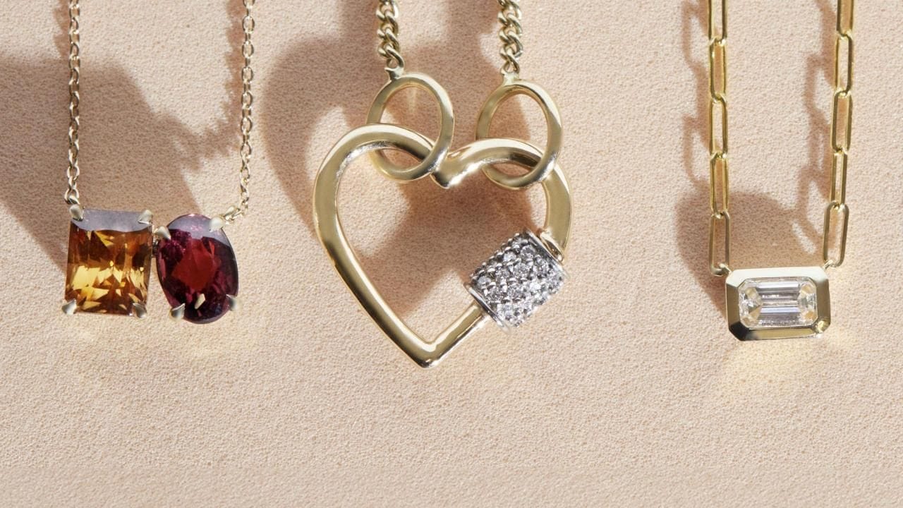 Three gold necklaces—featuring gleaming gemstones and heart-shaped and rectangular pendants—are displayed on a beige background, showcasing the beauty of shining jewelry when kept untangled and given proper jewelry care.