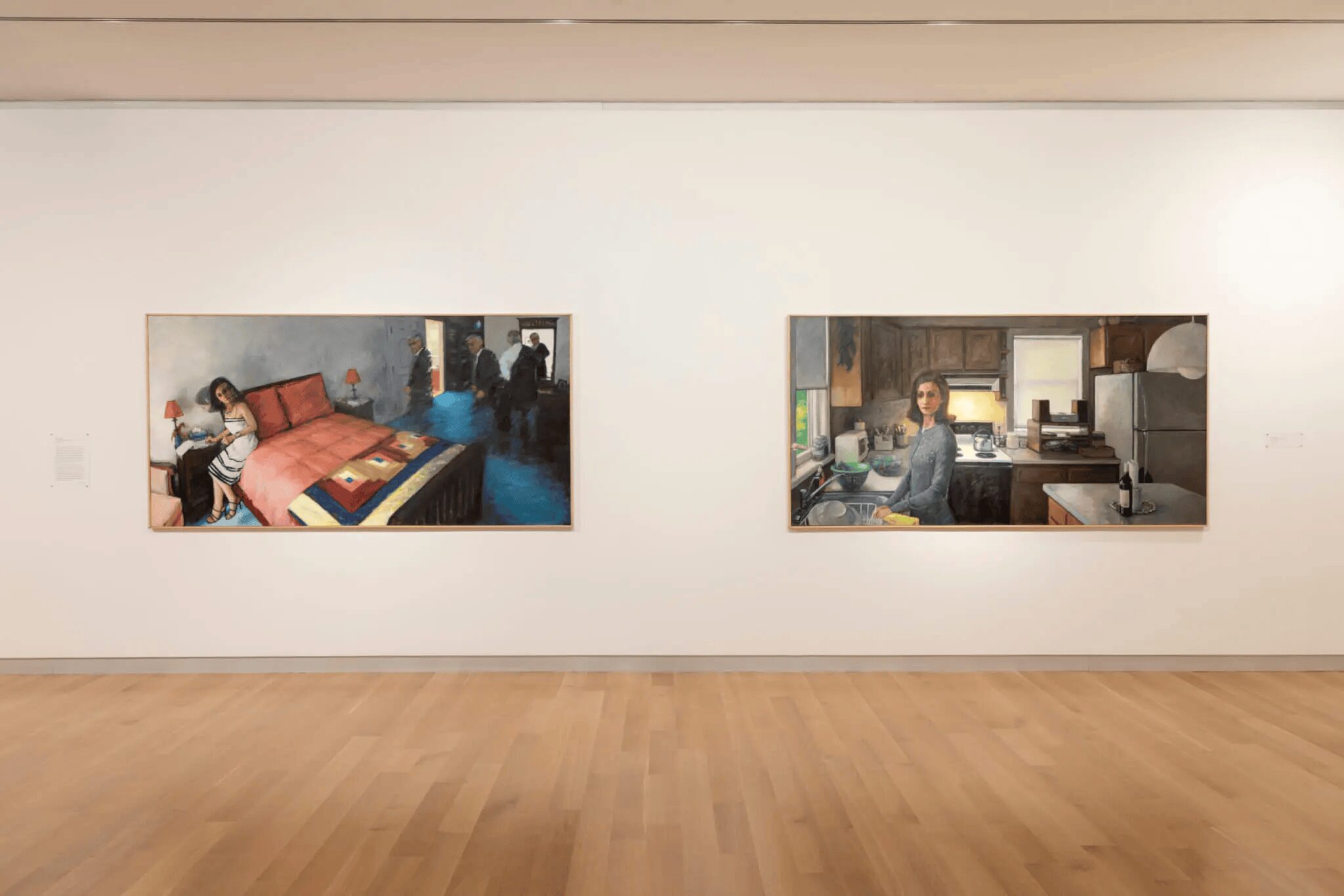 Two large paintings hang on a white gallery wall above a light wooden floor, evoking the spirit of New England. Both scenes, part of summer museum exhibitions, capture everyday life: people in a bedroom and a woman in a kitchen.