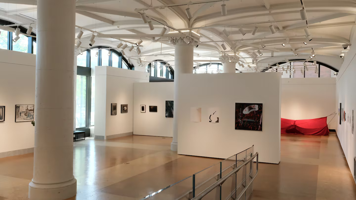 A modern art gallery with high ceilings, white walls, and large windows showcases photographs, paintings, and a striking red fabric installation—an inspiring stop for anyone exploring Boston weekend activities.
