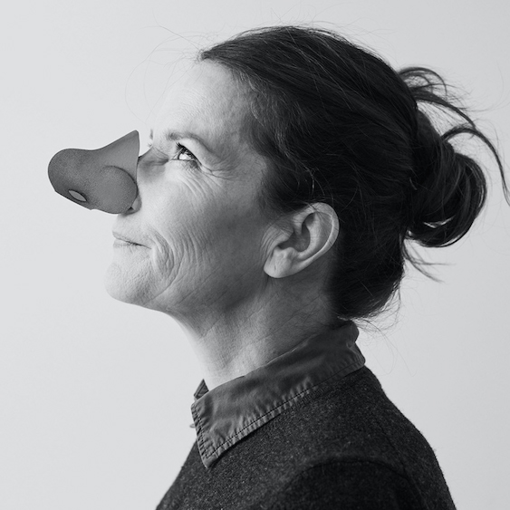 A grayscale photo of a woman in profile, wearing a dark top with her hair tied back, looking up and smiling slightly. She has a cartoonish animal nose prop attached to her nose—a quirky nod to the spirit of the Common Good Awards at MassArt.