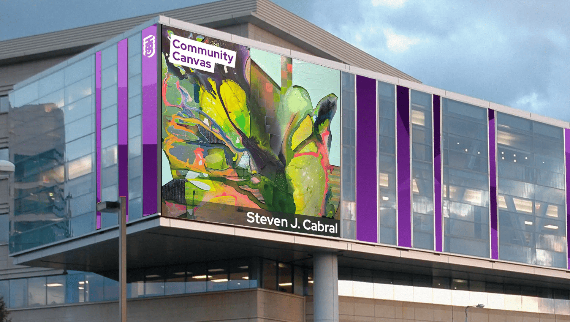 A modern glass building features a large digital display showing abstract, colorful artwork titled GBH Community Canvas by MassArt alum Steven J. Cabral. The exterior is accented by vertical purple panels.