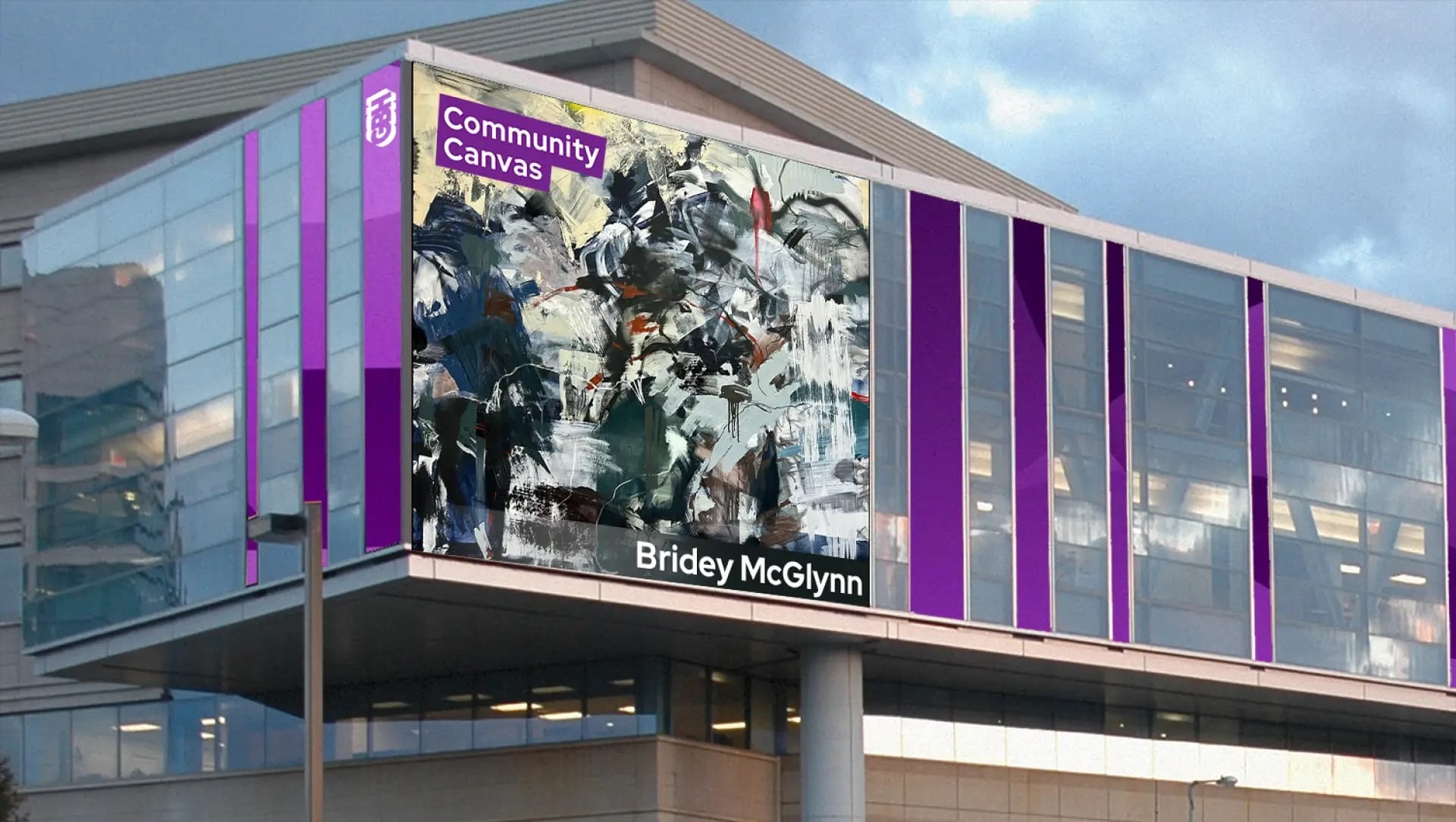 A modern building with glass panels and purple accents showcases a large abstract painting. The sign reads “Community Canvas” at the top and “Bridey McGlynn, MassArt Alum” at the bottom, highlighting this GBH Community Canvas installation.