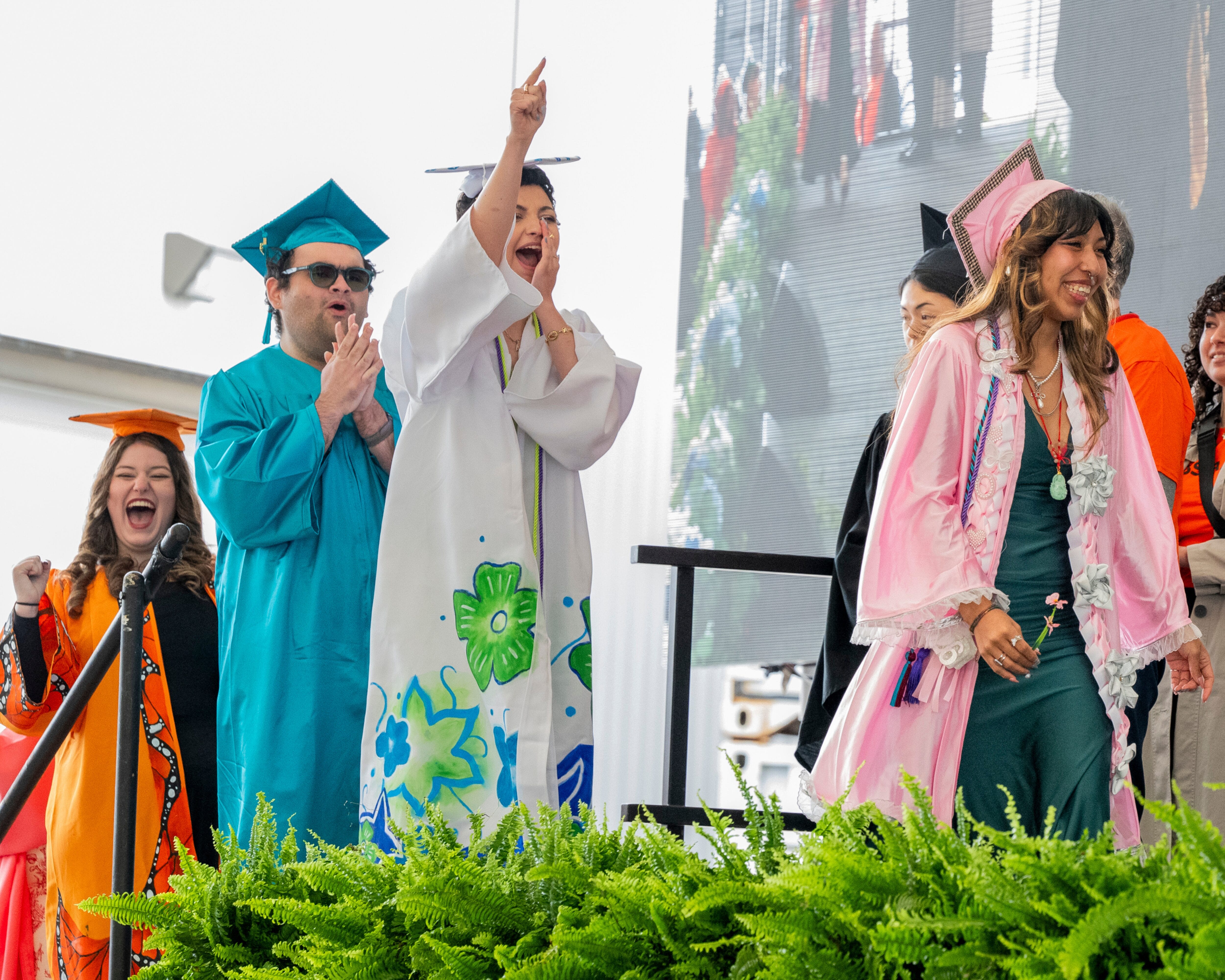 Graduates in colorful gowns cheer and celebrate while walking across the stage at MassArt Commencement.