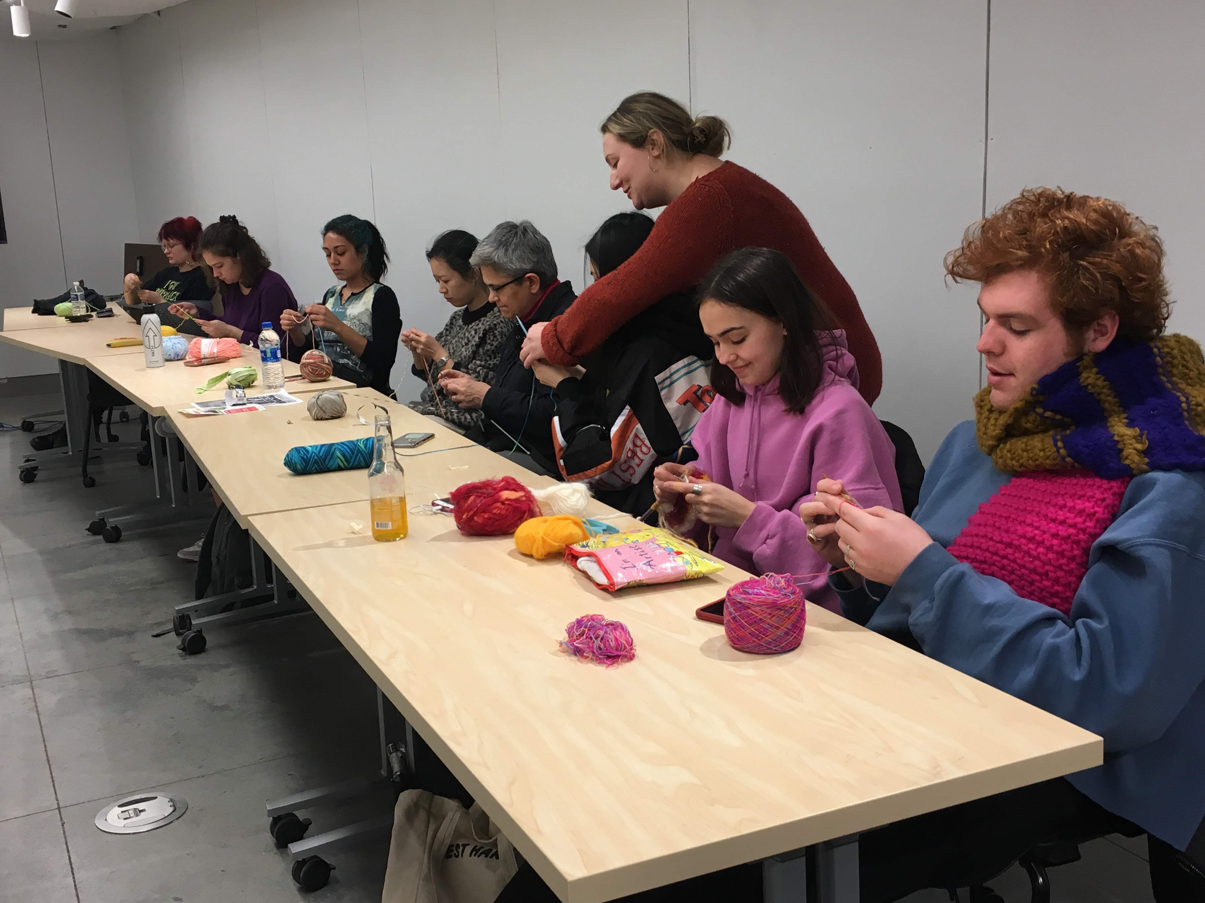 A group of people sit at tables, knitting and crocheting sustainable yarn in a classroom Sustainability Studio.