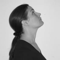 Woman in profile with dark hair in a ponytail, embodying Sustainability as she looks upward against a plain background.